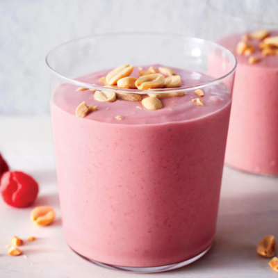 A cup of a pink smoothie in a glass with a peanut garnish