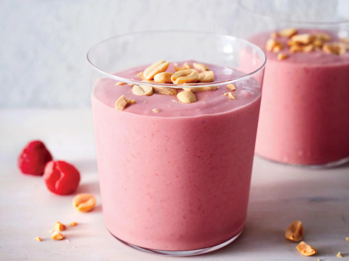 A cup of a pink smoothie in a glass with a peanut garnish