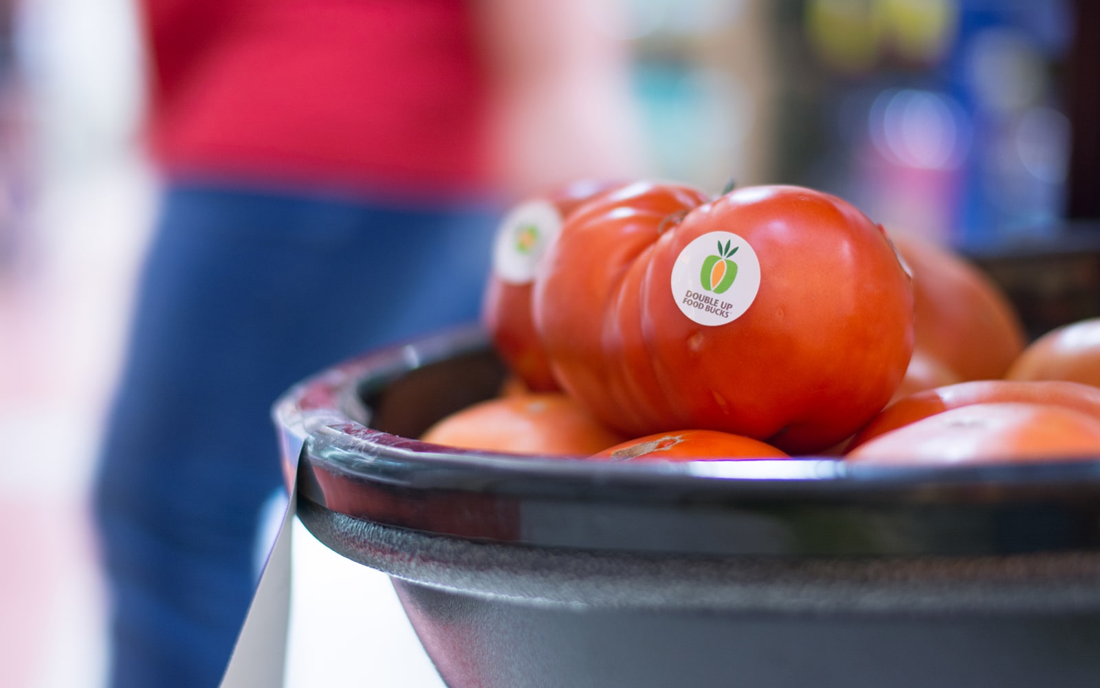 A basket of bright red tomatoes with Double Up Food Bucks stickers on them