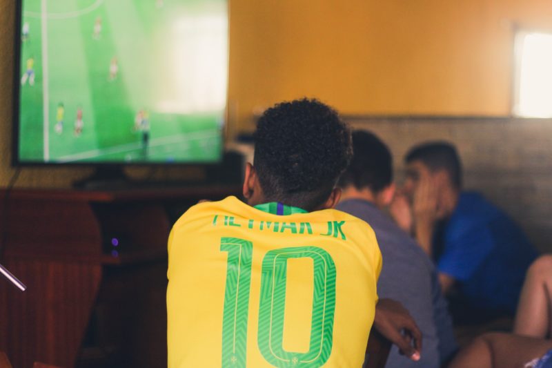 A boy wearing a green and yellow soccer jersey watching a soccer game on TV