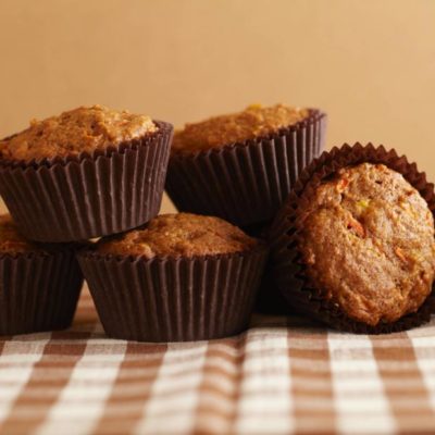 Five muffins sitting on a brown and white checkered table cloth