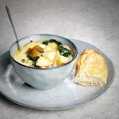 A gray bowl with potato and bacon soup in it and a baguette on the side