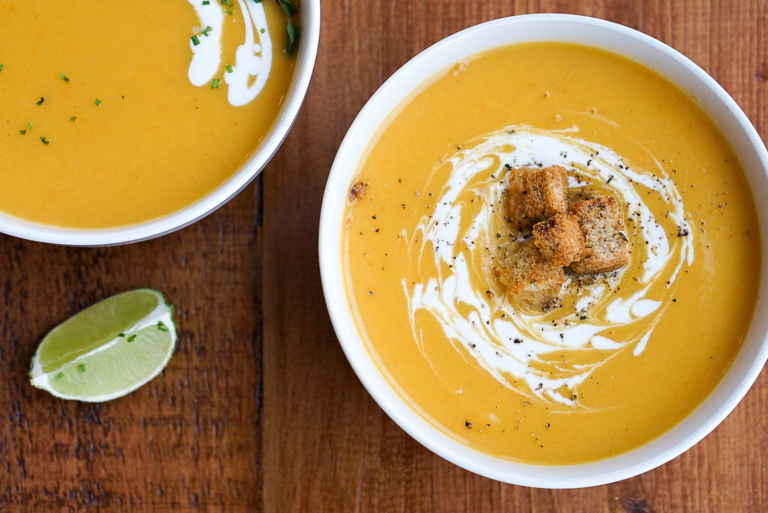 Two bowls of orange leek and potato soup with cream and a lime wedge