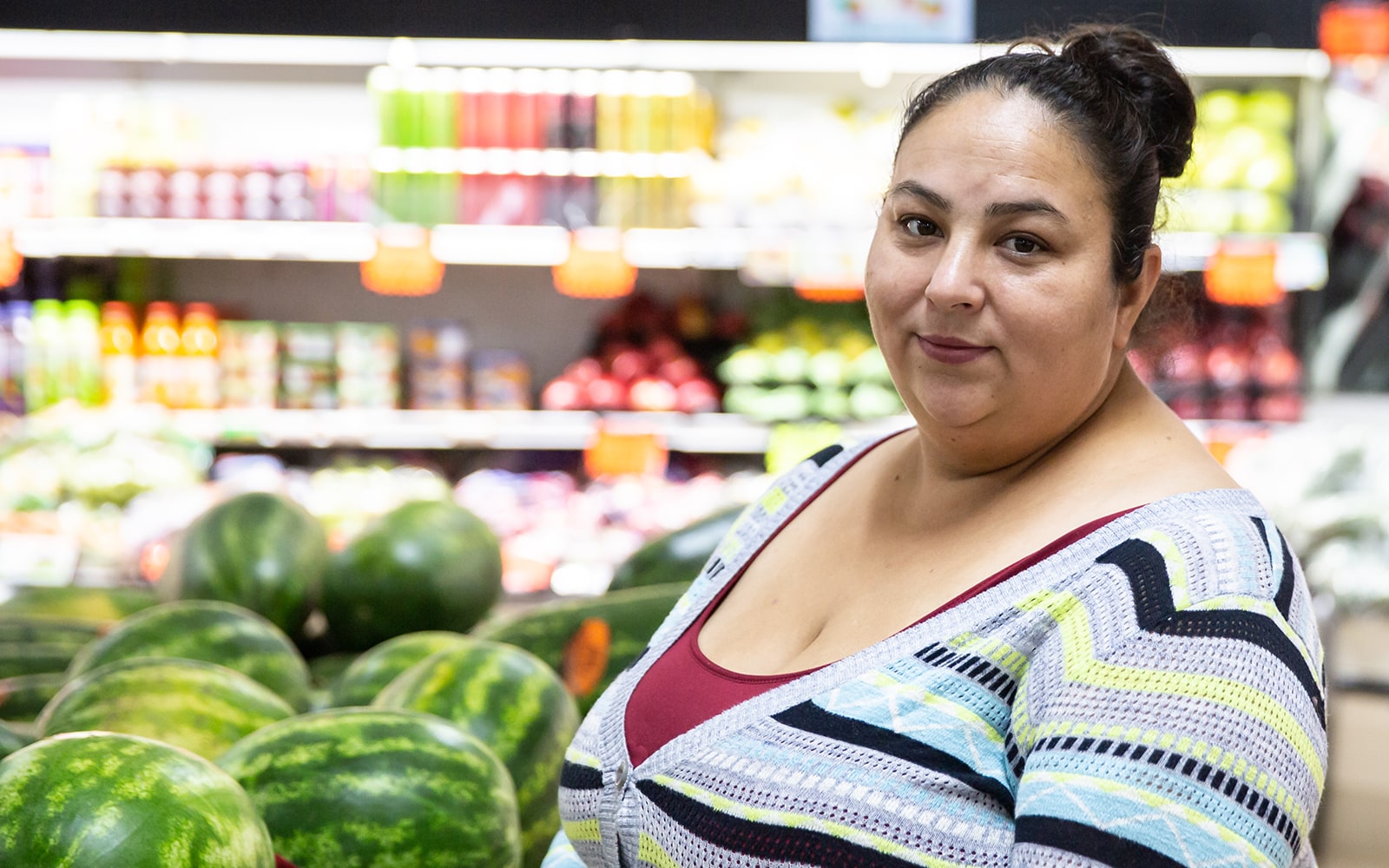 Miroslava, a woman wearing a red shirt and blue sweater standing in a grocery store near watermelons