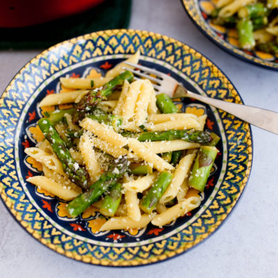 Two patterned bowls of pasta with asparagus and grated parmesan cheese.