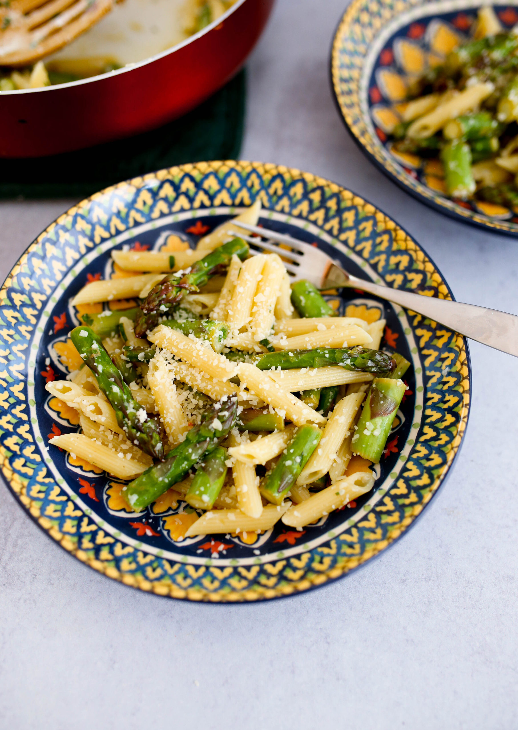 Two patterned bowls of pasta with asparagus and grated parmesan cheese.