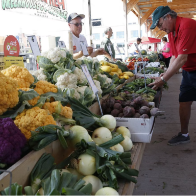 A shopper at the Flint Farmers Market picking out fresh produce from a vendor.