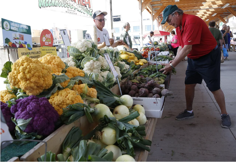 A shopper at the Flint Farmers Market picking out fresh produce from a vendor.
