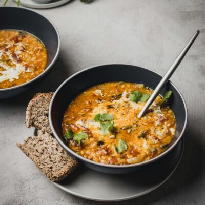 Two bowls of Mexican bean soup with fresh cheese and cilantro on plates with slices of wheat bread.