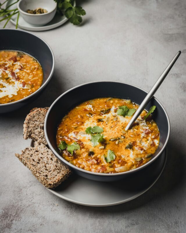 Two bowls of Mexican bean soup with fresh cheese and cilantro on plates with slices of wheat bread.