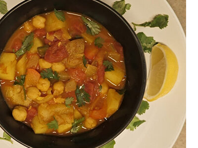 Black bowl filled with West Asian soup and fresh herbs on top of a white plate with more fresh herbs and lemon wedges.