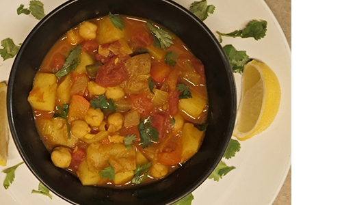 Black bowl filled with West Asian soup and fresh herbs on top of a white plate with more fresh herbs and lemon wedges.